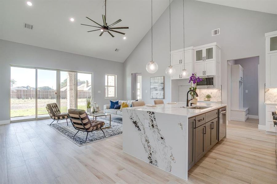 Kitchen featuring high vaulted ceiling, glass insert cabinets, light stone counters, white cabinets, and a ceiling fan