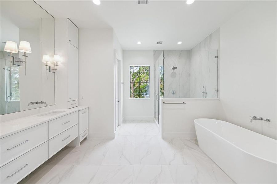 The walk-in shower is a luxurious retreat with seamless glass walls and door, accented by designer chrome plumbing fixtures. The custom white oak vanity with double sinks exudes sophistication, paired with a sleek wall-mounted designer chrome faucet. Designer sconce lighting enhances the elegance, creating a serene and opulent bathroom experience.