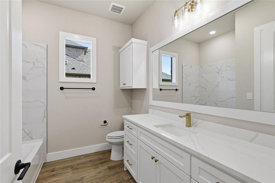 Bathroom featuring a spacious white vanity with a single sink, gold-finish faucet, and a large mirror