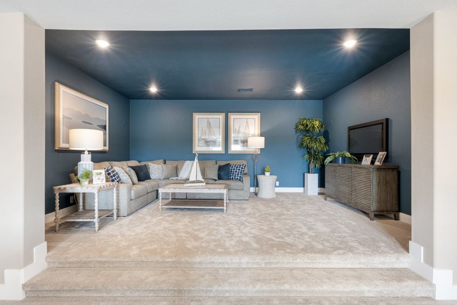 Sunken living room with blue accent walls, gray sectional sofa, and TV console on carpet flooring