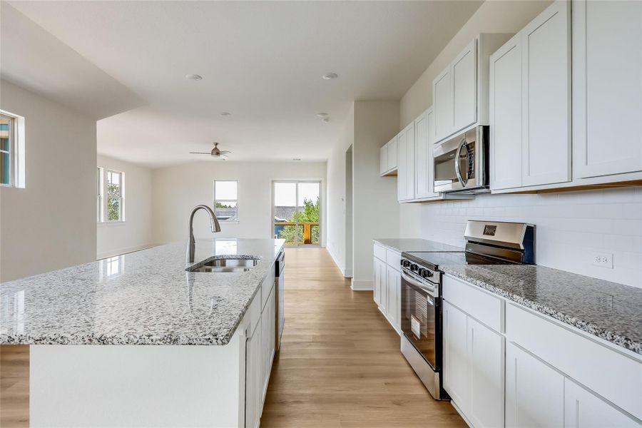 Kitchen with stainless steel appliances, white cabinetry, light wood-style floors, light stone counters, and a kitchen island with sink