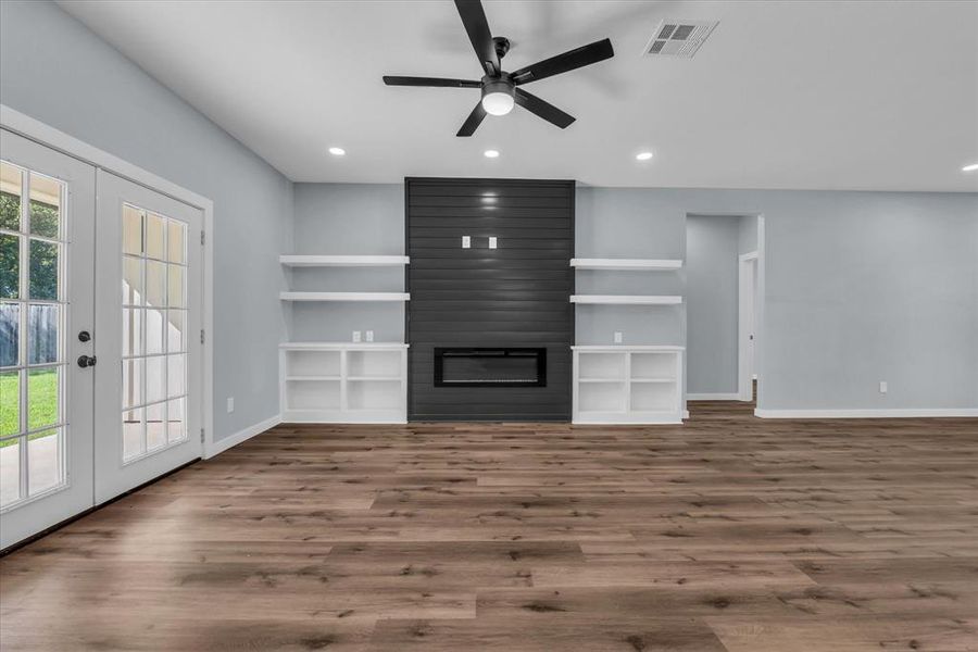 Unfurnished living room with a large fireplace, french doors, wood finished floors, and recessed lighting Unfurnished living room with a large fireplace, french doors, wood finished floors, and recessed lighting
