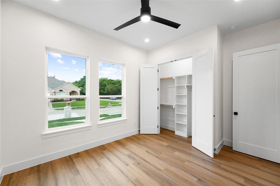 Spacious room featuring wood-finish flooring, two large windows, a built-in closet system, a ceiling fan with integrated lighting, and recessed ceiling lights