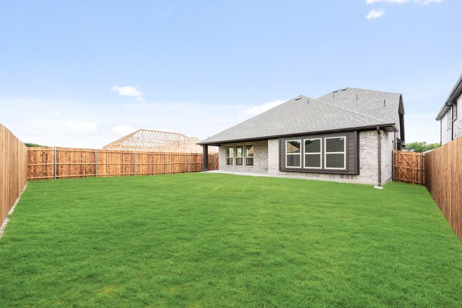 Backyard of brick home with large green lawn, wood privacy fence, and covered patio area.