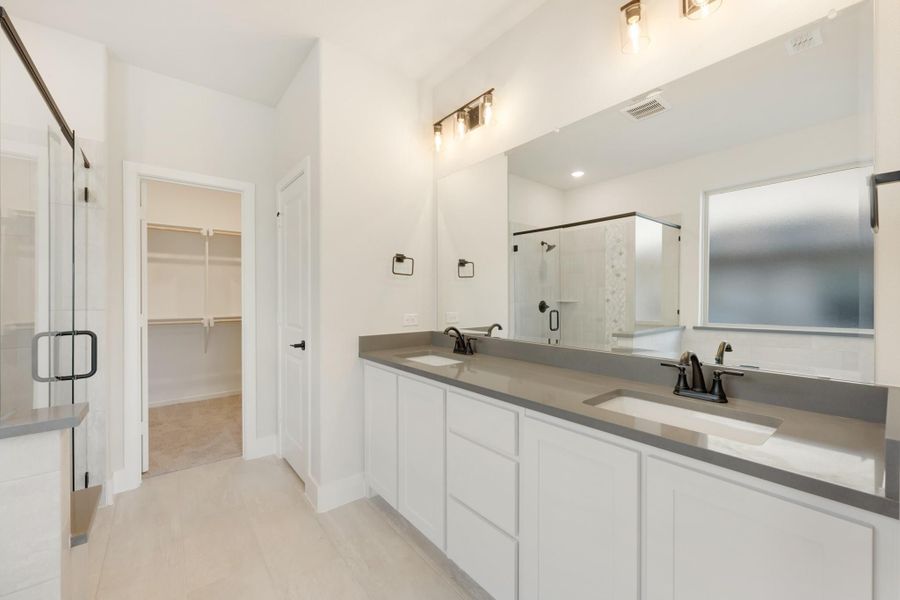 Master bathroom with double vanity, gray countertops, glass shower, and walk-in closet entrance Master bathroom with double vanity, gray countertops, glass shower, and walk-in closet entrance
