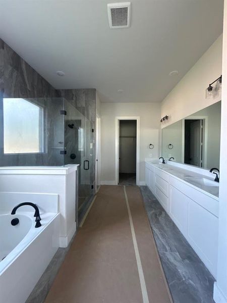 Spacious bathroom featuring a white soaking tub, frameless glass shower enclosure with dark-toned tile surround, dual vanities with white cabinetry, and matte black fixtures Spacious bathroom featuring a white soaking tub, frameless glass shower enclosure with dark-toned tile surround, dual vanities with white cabinetry, and matte black fixtures