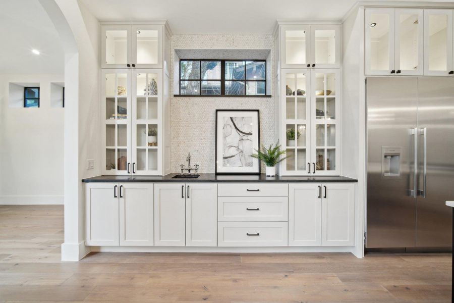 Bar featuring a sink, arched walkways, stainless steel built in refrigerator, and light wood finished floors