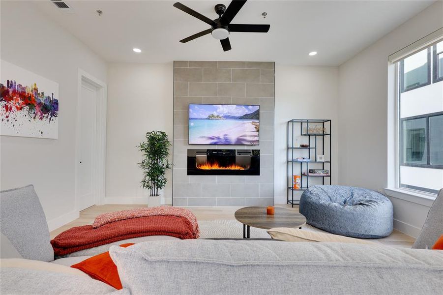 Living room featuring ceiling fan, a tiled fireplace, and hardwood / wood-style floors