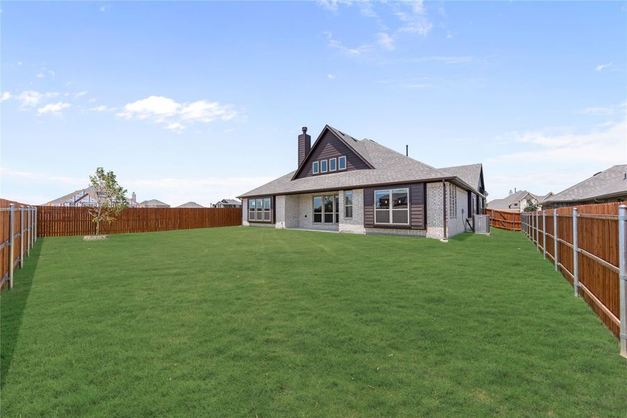 Backyard view of single-story brick home with large grassy lawn and wood privacy fence Backyard view of single-story brick home with large grassy lawn and wood privacy fence