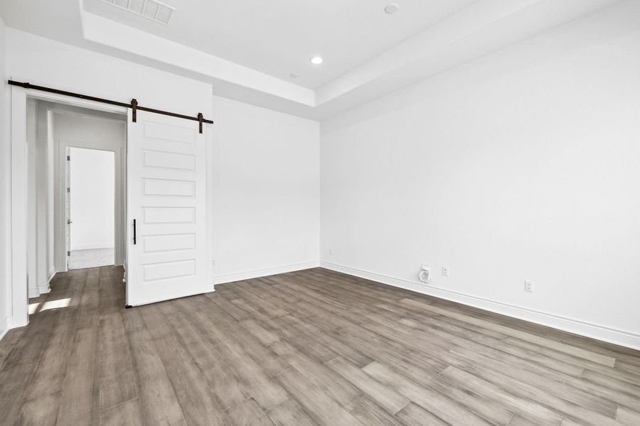 Unfurnished room featuring a barn door, wood finished floors, a raised ceiling, and recessed lighting