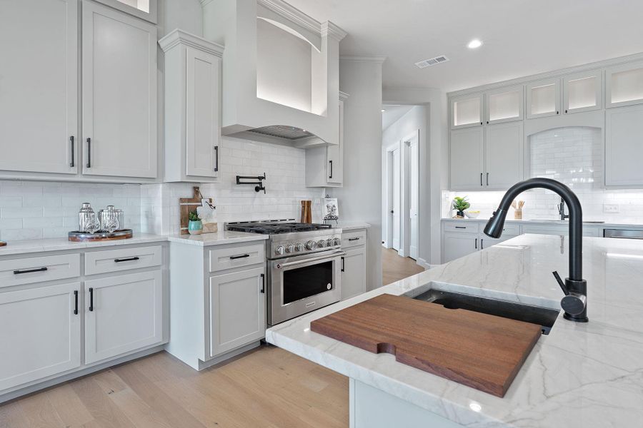 Kitchen featuring stainless steel range, custom exhaust hood, tasteful backsplash, white cabinets, and light wood-style flooring