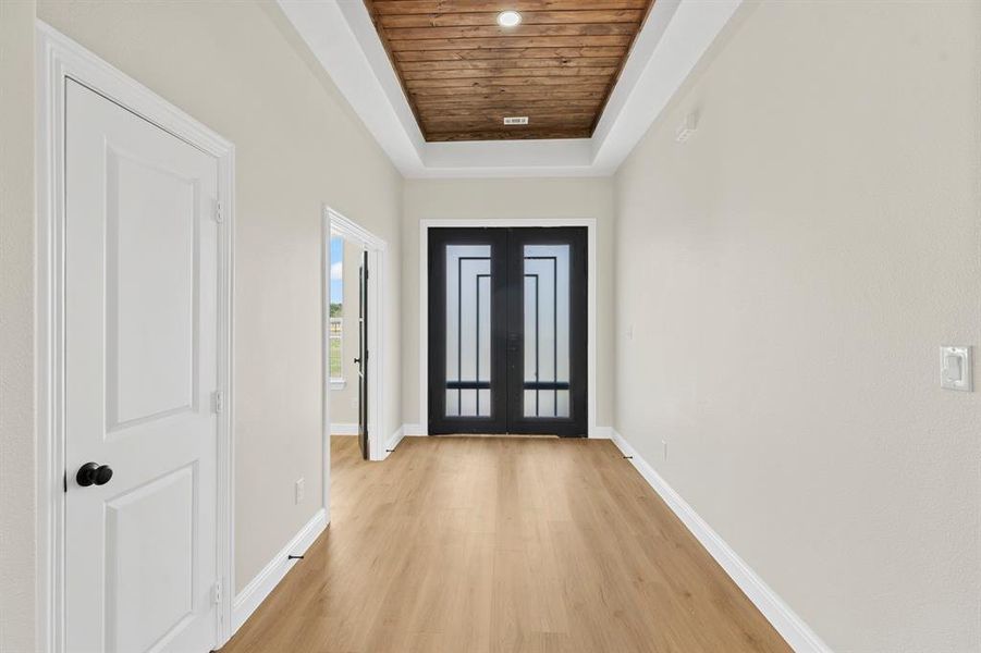 Entryway featuring a raised ceiling, light wood-style flooring, french doors, and wooden ceiling