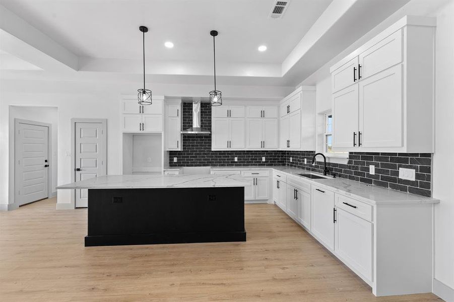Kitchen with a center island, hanging light fixtures, light stone counters, dark cabinetry, and a tray ceiling