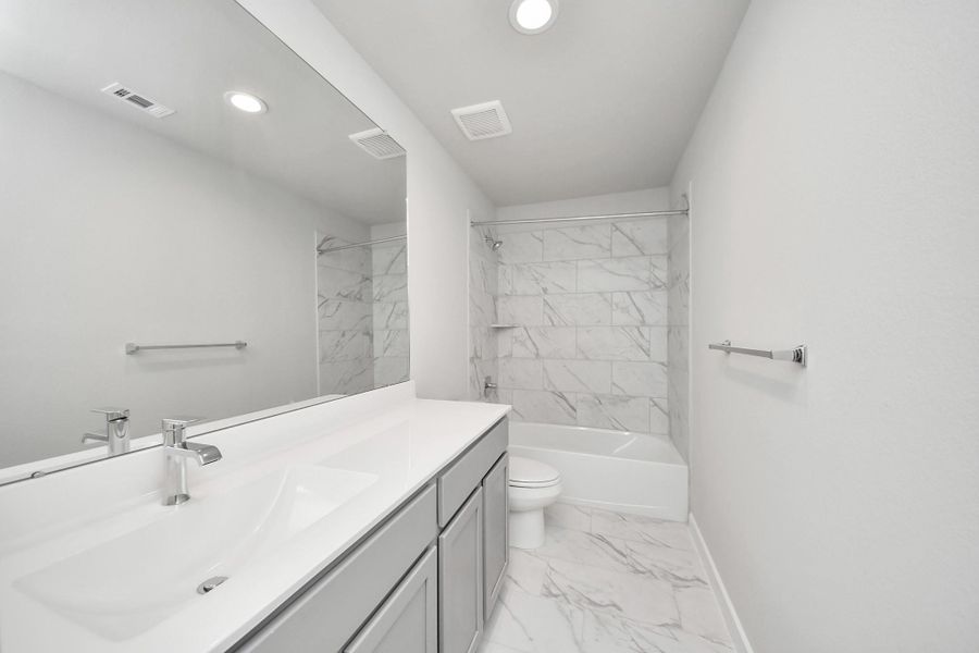 Secondary bath features tile flooring, bath/shower combo with tile surround, light stained wood cabinets, beautiful light countertop. Sample photo of completed home with similar floor plan. Actual colors and selections may vary.