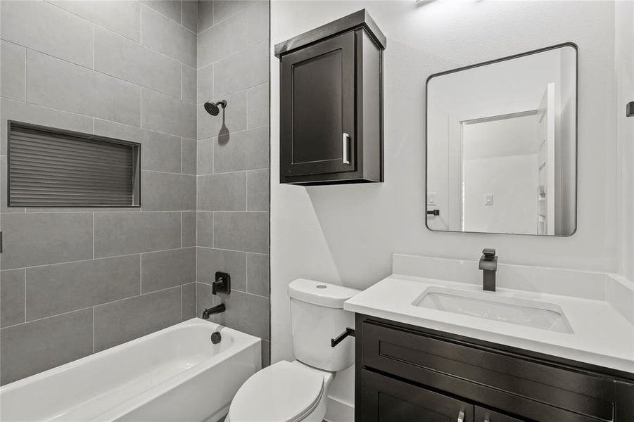 Full bathroom with vanity, tiled shower / bath combo, and toilet