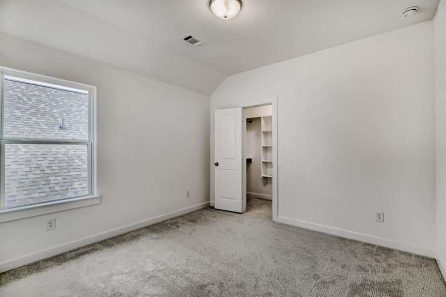 Unfurnished bedroom featuring a walk in closet, carpet floors, and lofted ceiling