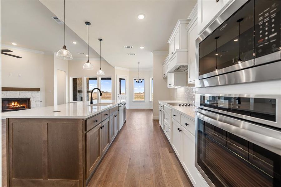 Kitchen with white cabinets, stainless steel appliances, a stone fireplace, decorative light fixtures, and dark wood-style floors
