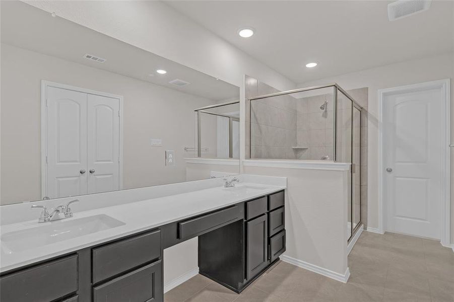 This is a spacious Primary restroom, modern bathroom featuring a dual sink vanity with ample storage, a large mirror, a walk-in shower with glass enclosure, and neutral color tones. There are recessed lights and a door leading to the toilet.