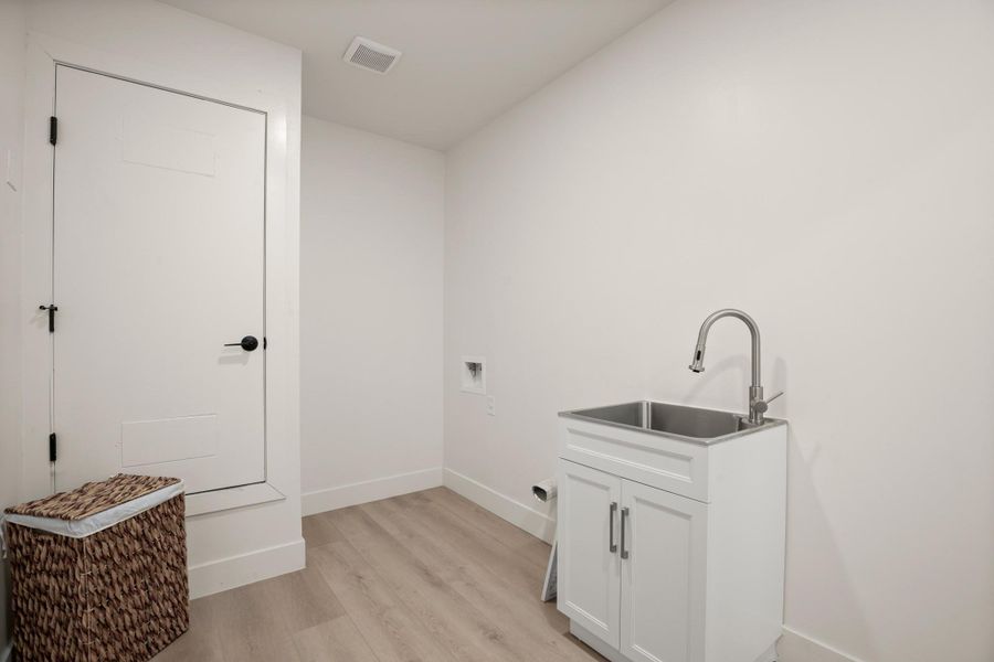 Laundry room with light wood-type flooring, washer hookup, and cabinet space