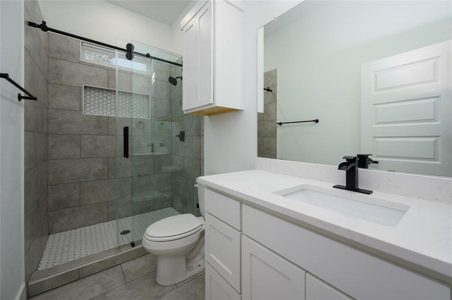 Bathroom with vanity, a shower with door, tile patterned floors, and toilet