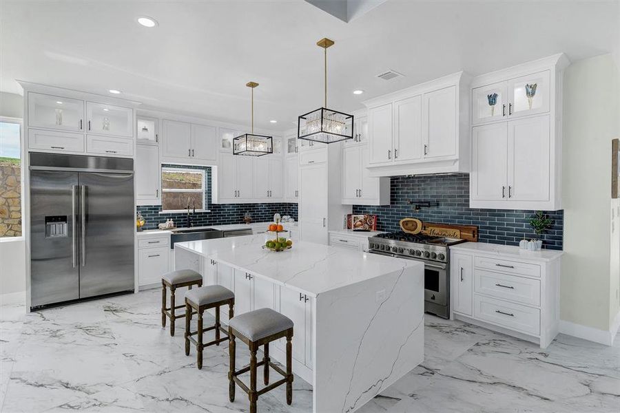 Kitchen featuring high end appliances, a kitchen island, white cabinets, and decorative light fixtures