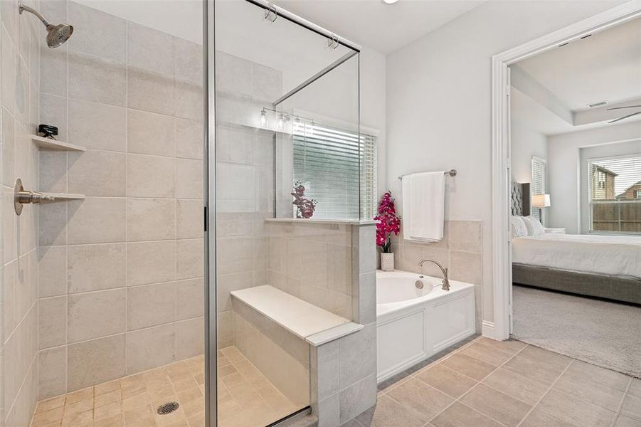 Spacious bathroom featuring a glass-enclosed shower with a built-in bench and shelving, a separate soaking tub, and tile flooring