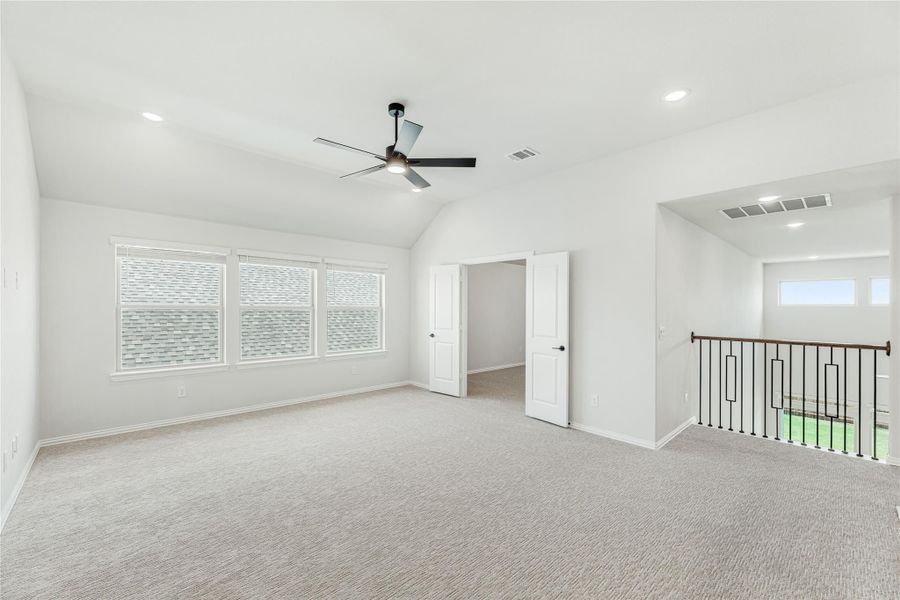 Spacious upstairs room with vaulted ceiling, ceiling fan, carpet flooring, and open staircase railing nearby.