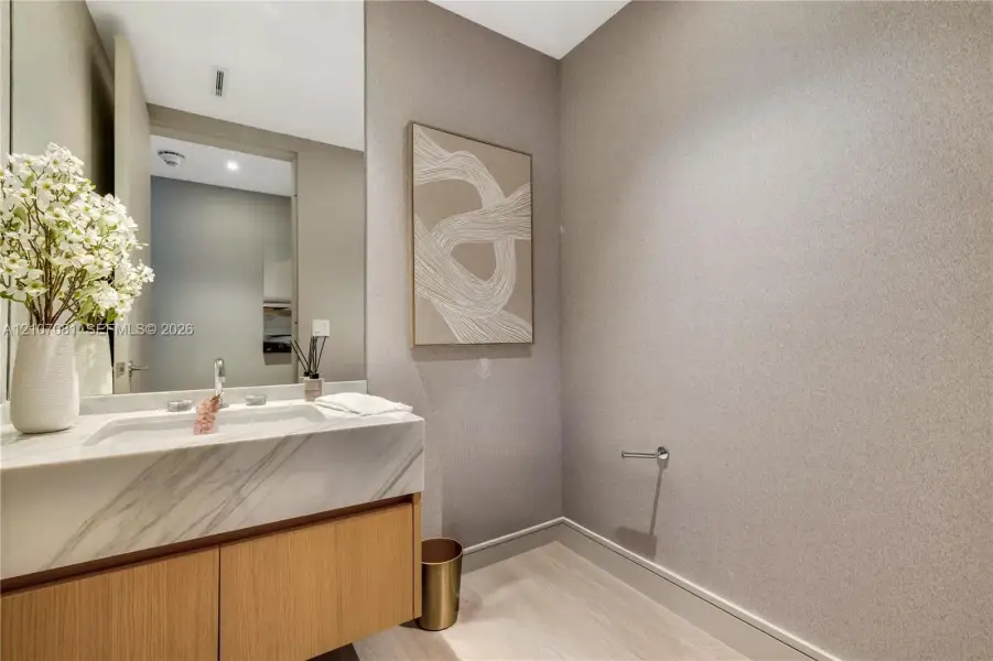 Floating vanity with light wood-finish cabinetry, stone countertop featuring integrated sink, polished metal faucet, and textured wall finish Floating vanity with light wood-finish cabinetry, stone countertop featuring integrated sink, polished metal faucet, and textured wall finish