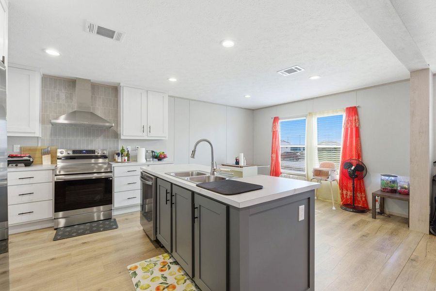 Kitchen featuring stainless steel appliances, two tone color scheme, light wood-style floors, light countertops, and an island with sink