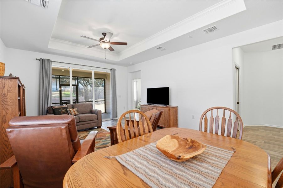 Dining space with a ceiling fan, light wood-type flooring, and a raised ceiling