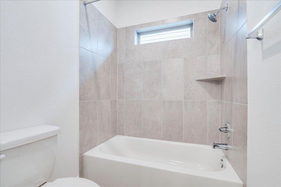 Jack and Jill Bathroom featuring a white bathtub with a tiled surround, a built-in shower niche, and a window for natural light