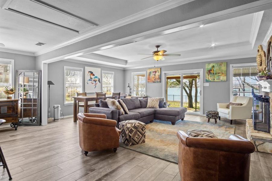 Living room with a tray ceiling, light hardwood / wood-style flooring, ornamental molding, and ceiling fan