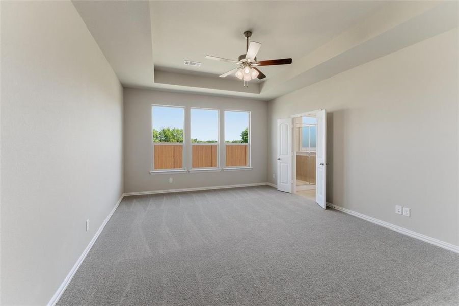 Unfurnished bedroom with light colored carpet, connected bathroom, ceiling fan, and a tray ceiling
