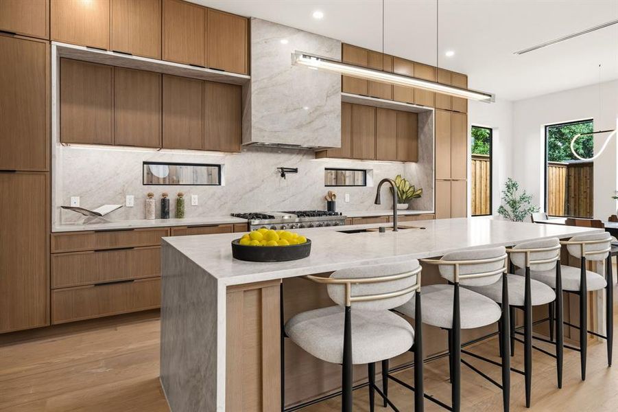 Contemporary kitchen featuring a waterfall-edge island, integrated appliances, wood-finish cabinetry, a full-height stone slab backsplash, and wood-finish flooring
