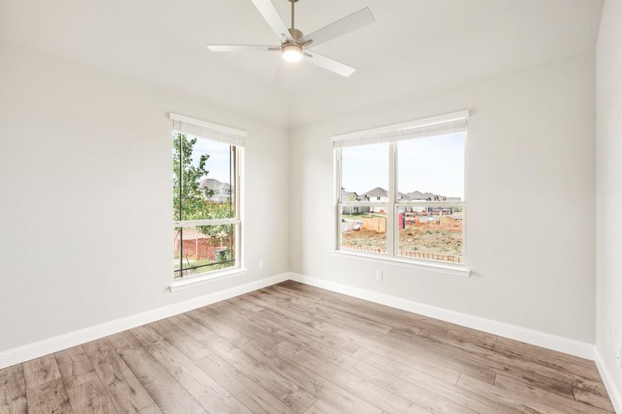 Empty bedroom with light wood floors, ceiling fan, and two windows overlooking a neighborhood Empty bedroom with light wood floors, ceiling fan, and two windows overlooking a neighborhood
