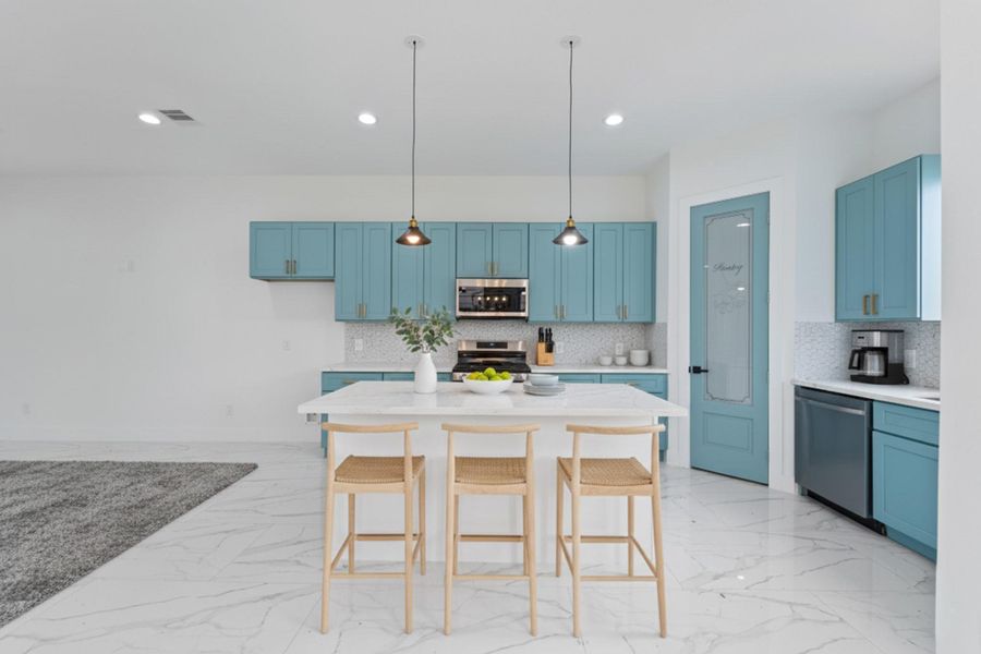 This view shows the main kitchen wall with a full bank of upper and lower blue cabinets and a white backsplash and countertop.