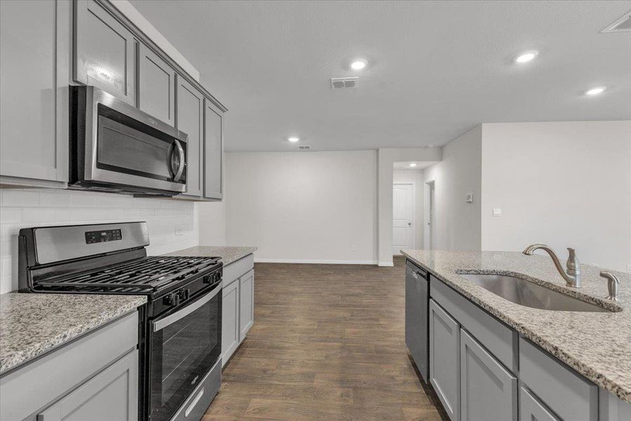 The kitchen features grey cabinetry, stainless steel appliances, and light-colored granite countertops with a white subway tile backsplash