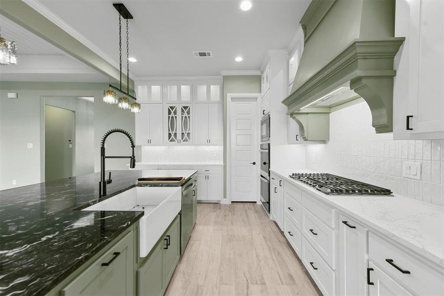 Kitchen featuring dark stone counters, light hardwood / wood-style flooring, decorative light fixtures, white cabinetry, and stainless steel appliances