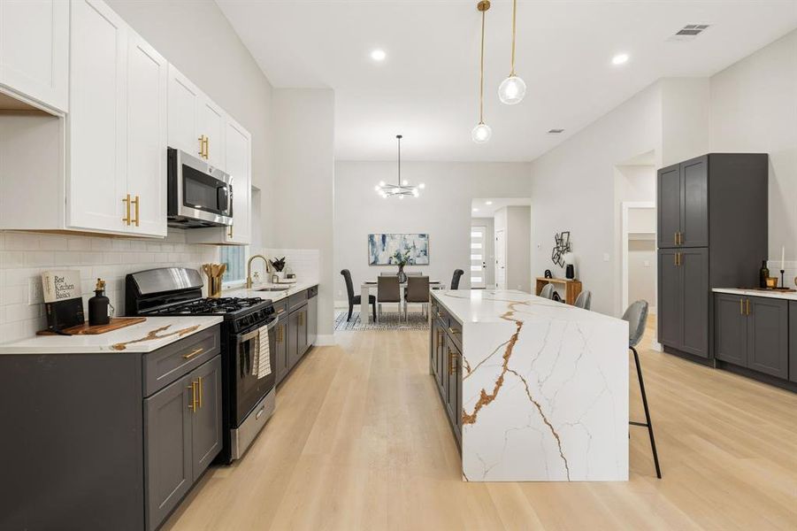 Open-concept kitchen with a large waterfall island featuring distinctive veining, light wood-finish flooring, and recessed lighting Open-concept kitchen with a large waterfall island featuring distinctive veining, light wood-finish flooring, and recessed lighting