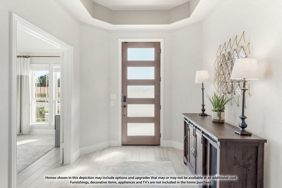 Bright home entryway with wood front door, tray ceiling, and dark wood console table with lamps Bright home entryway with wood front door, tray ceiling, and dark wood console table with lamps