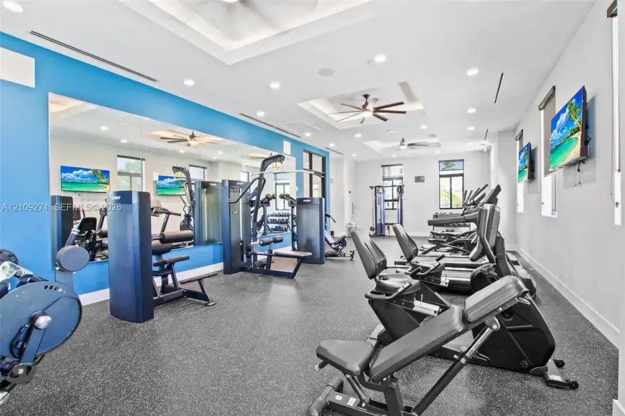 Fitness center featuring rubber flooring, recessed ceiling lighting, tray ceilings with integrated fans, and a floor-to-ceiling wall mirror