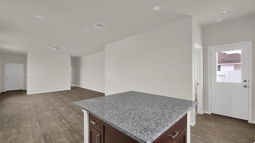 Kitchen featuring dark wood finish cabinetry, dark wood finished floors, light stone counters, a kitchen island, and recessed lighting
