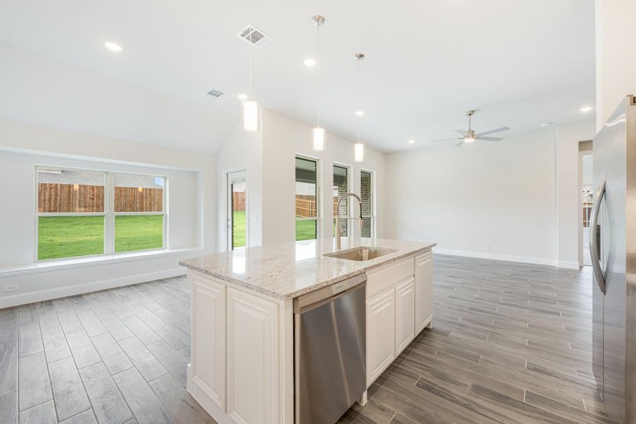 Kitchen island with granite countertop, sink, and stainless steel dishwasher, open to living area with backyard views