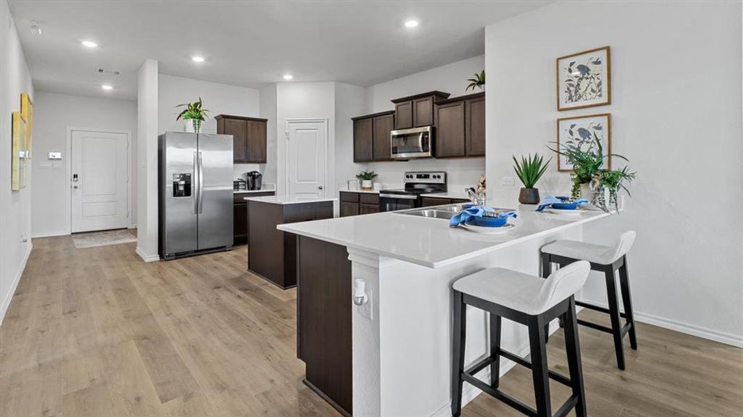 Kitchen with stainless steel appliances, dark wood finish cabinets, a peninsula, a breakfast bar area, and light wood-style floors Kitchen with stainless steel appliances, dark wood finish cabinets, a peninsula, a breakfast bar area, and light wood-style floors