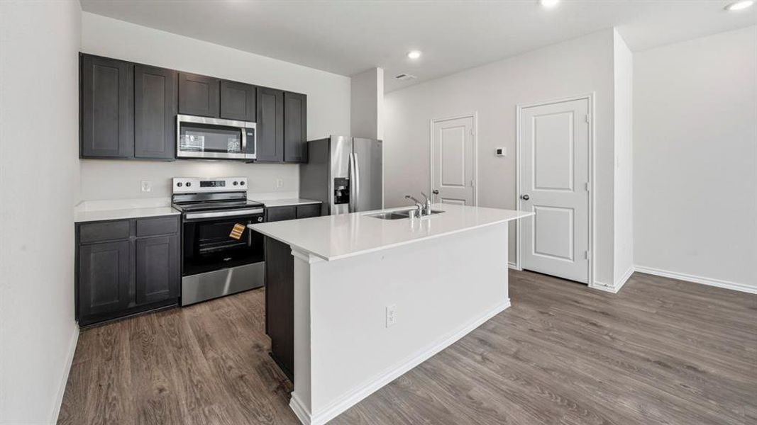Kitchen with stainless steel appliances, a kitchen island with sink, dark wood-style floors, and recessed lighting