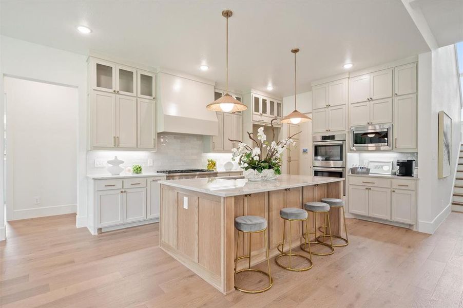 Kitchen featuring custom range hood, tasteful backsplash, light wood-type flooring, a kitchen island, and stainless steel appliances