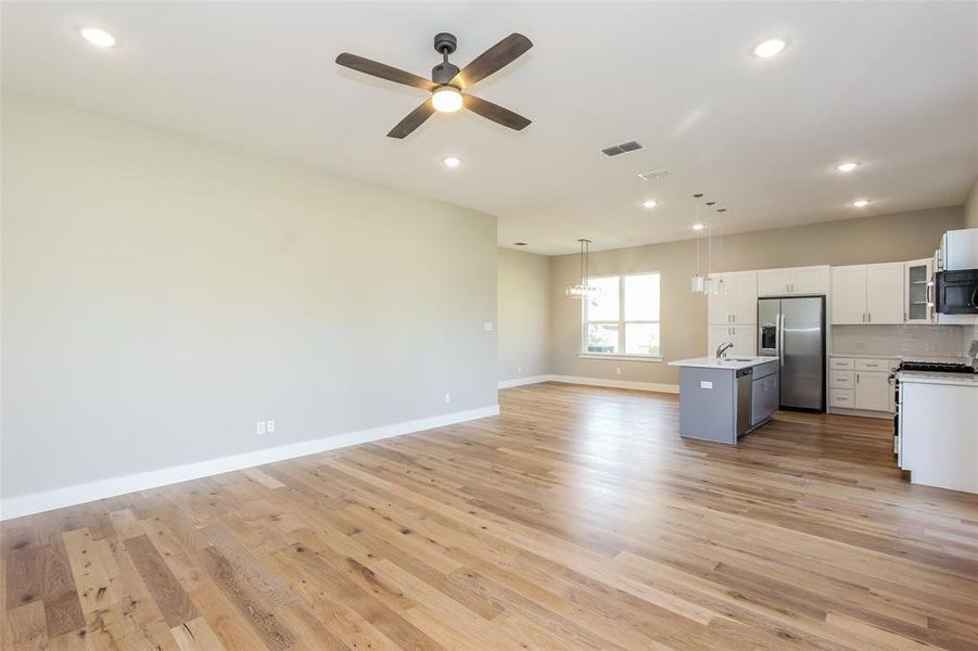 Kitchen with sink, hanging light fixtures, stainless steel appliances, a center island, and light wood-type flooring