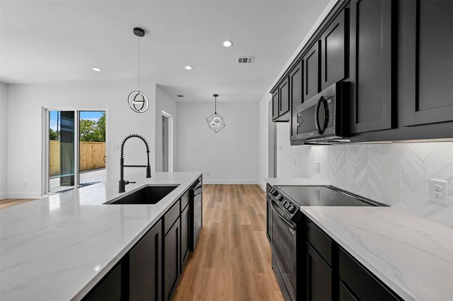 Kitchen featuring backsplash, stainless steel appliances, sink, light wood-type flooring, and hanging light fixtures