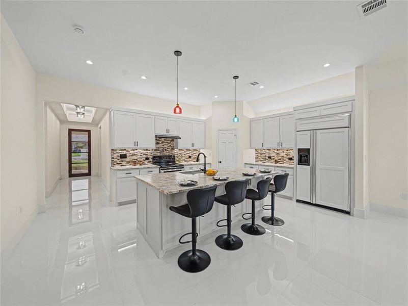 Kitchen with paneled built in refrigerator, a kitchen breakfast bar, stainless steel range with electric stovetop, light stone countertops, and hanging light fixtures