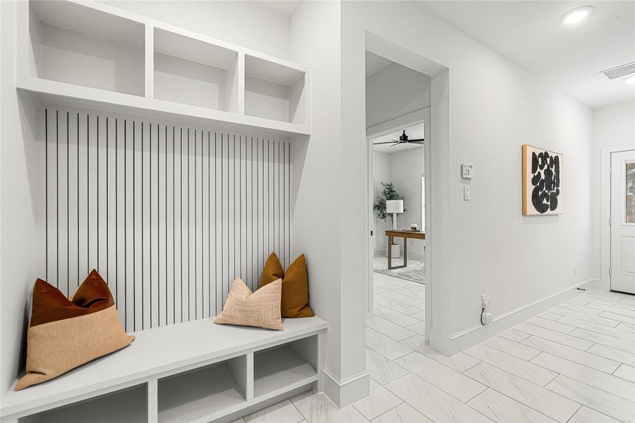 Welcoming foyer with built-in bench seating and storage cubbies. The space features sleek tile flooring, recessed lighting, and a view into an first floor room with stylish decor.